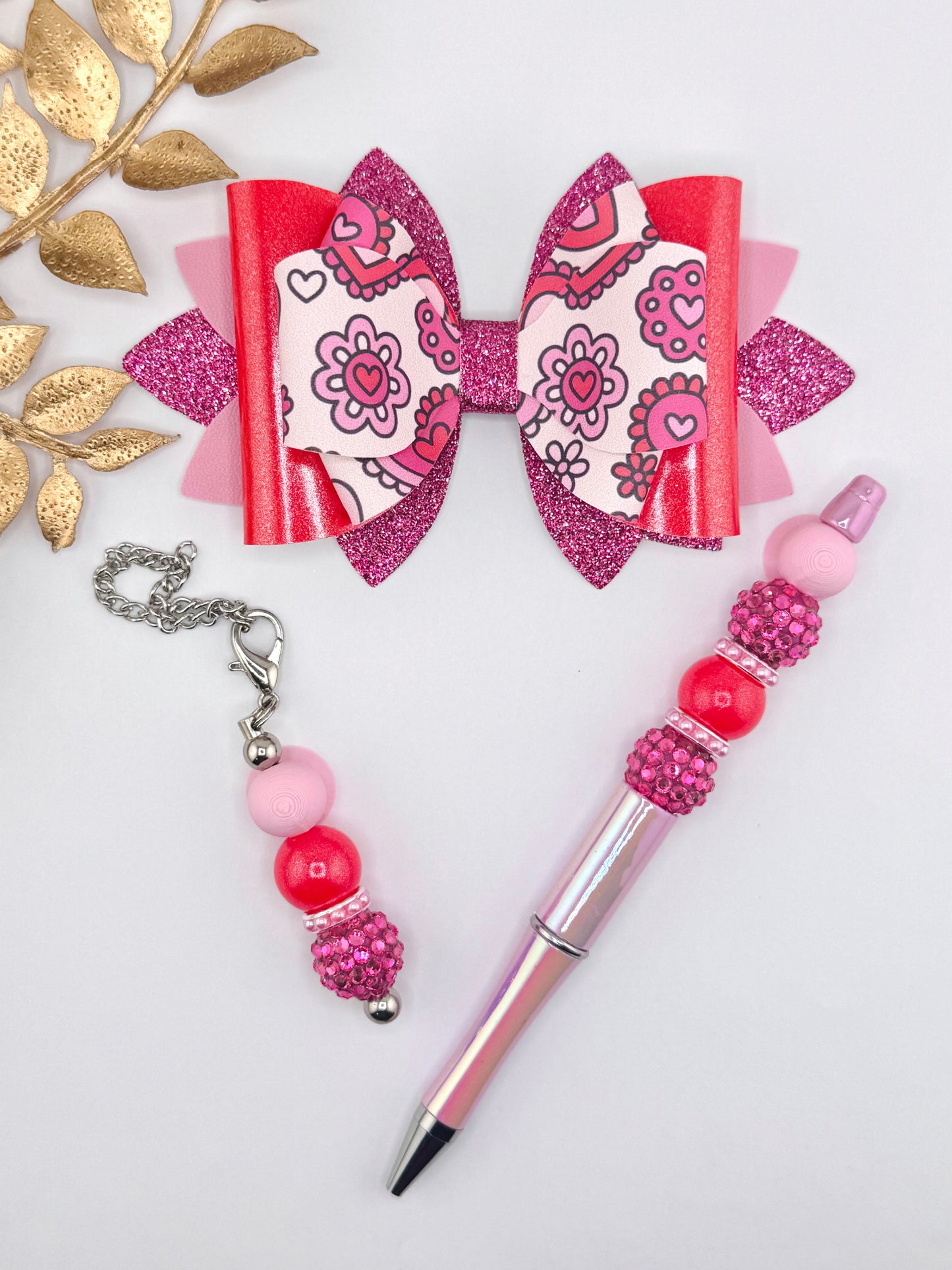Pink and red floral heart faux leather bow kit featuring a glitter layered bow, beaded pen, and matching beaded charm on a white background