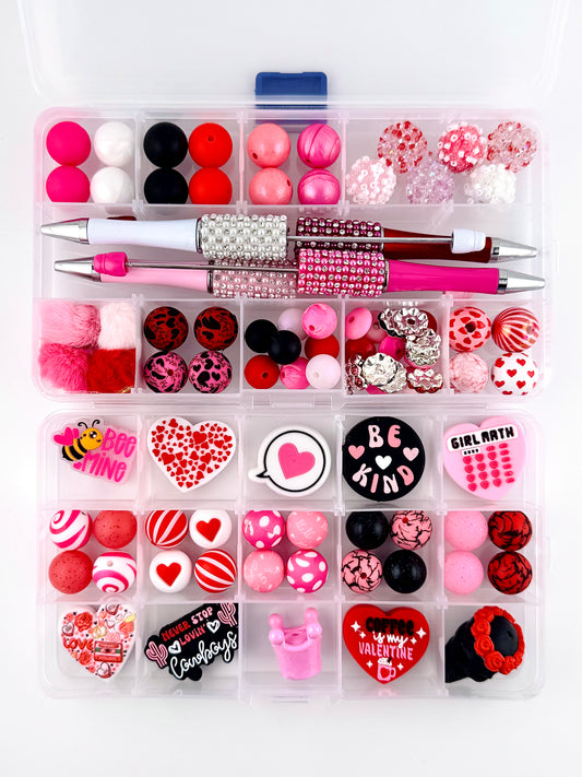 “92 piece Valentine’s Day bead starter kit featuring pink, red, white, and black silicone beads, heart-themed acrylic focals, rhinestone pens, pom poms, and Valentine charms arranged in a clear organizer box”