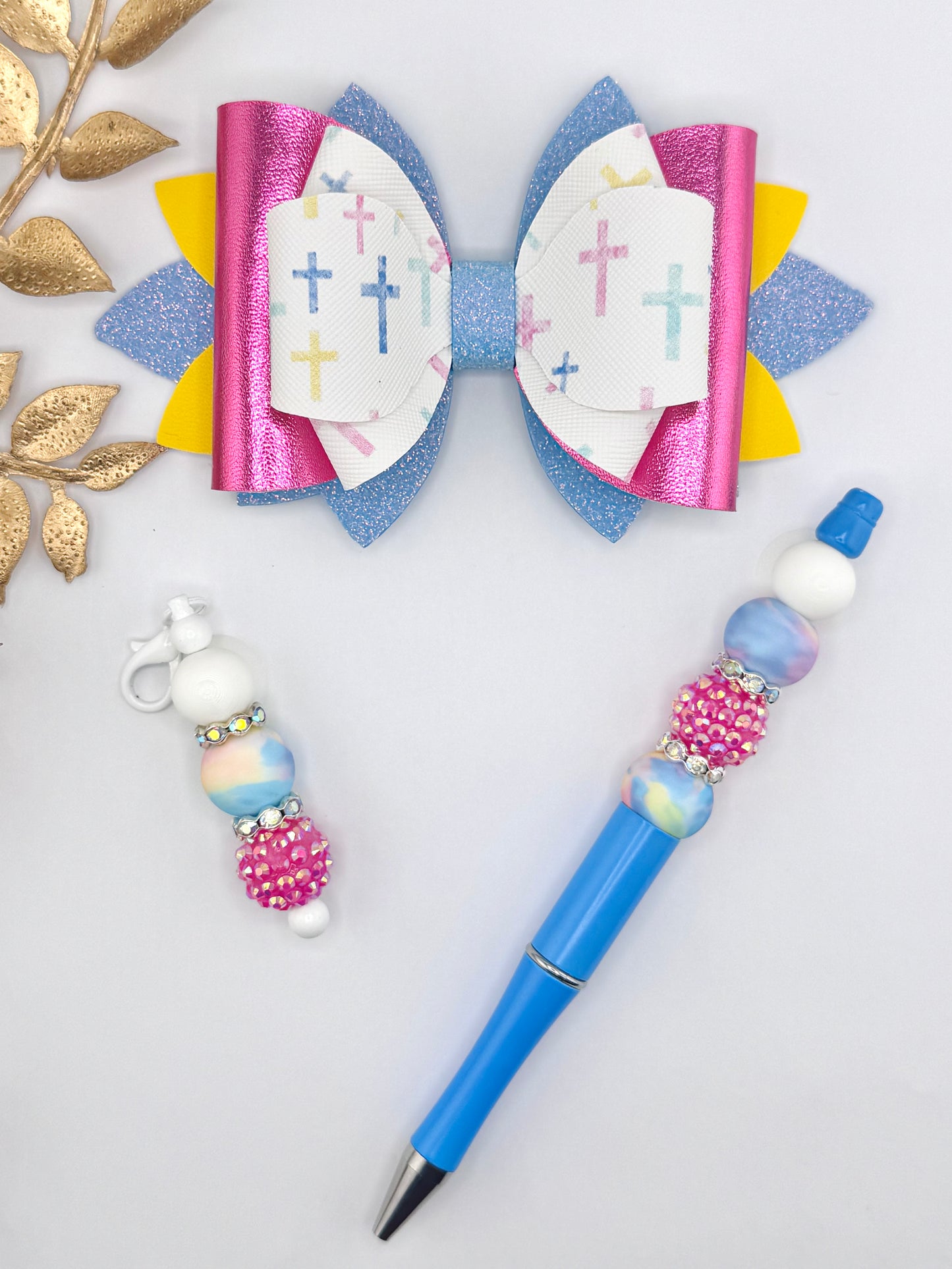 Pastel faux leather bow kit featuring blue glitter, pink metallic, yellow layers, and a white pastel cross print bow, shown with matching beaded pen and charm accessories