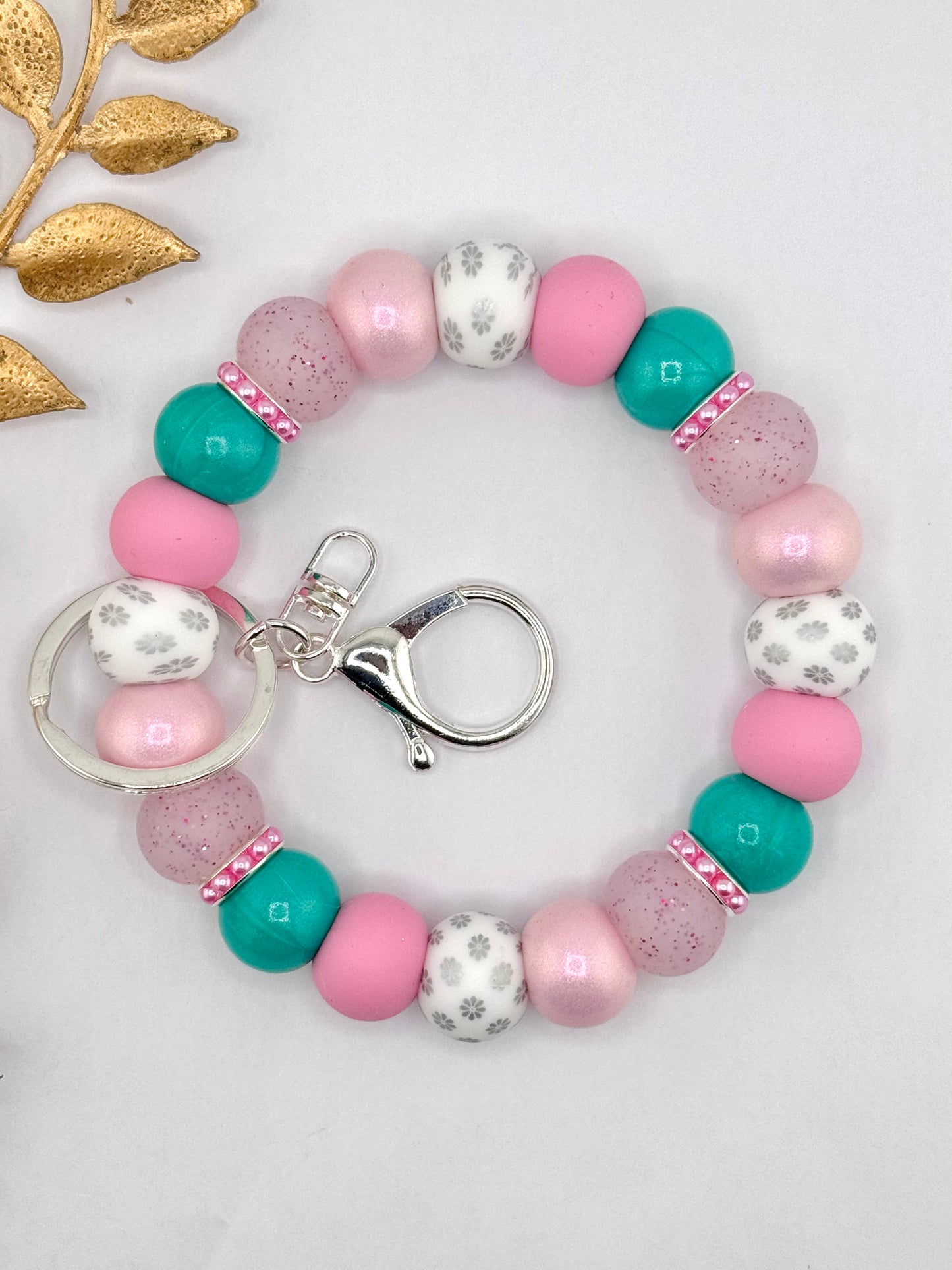 Pink and teal silicone bead keychain wristlet with white floral printed beads, speckled beads, and silver clasp hardware.
