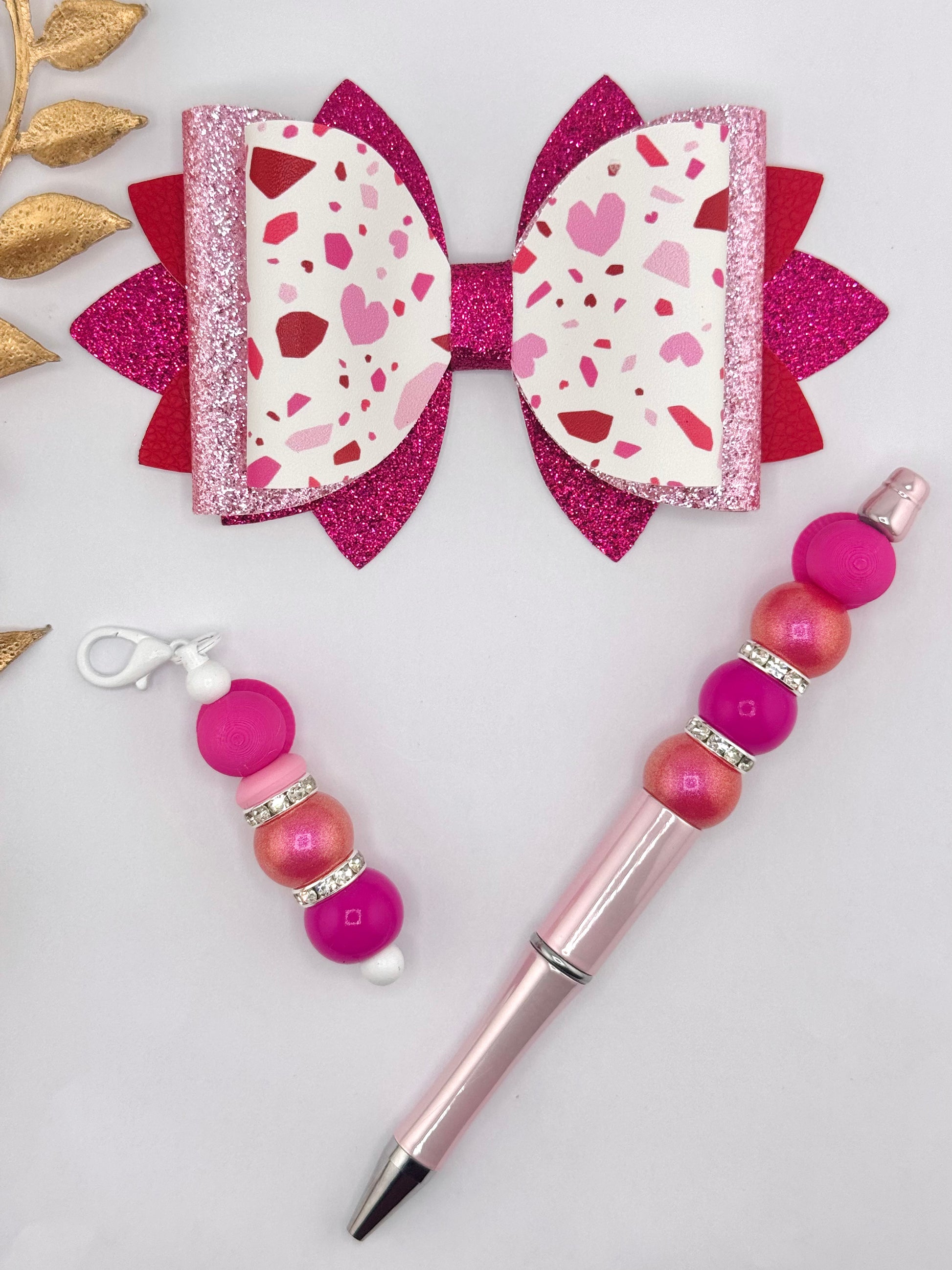 Pink terrazzo heart faux leather bow with layered hot pink and red glitter backing, Valentine-inspired handmade hair bow displayed with matching beaded pen and keychain.