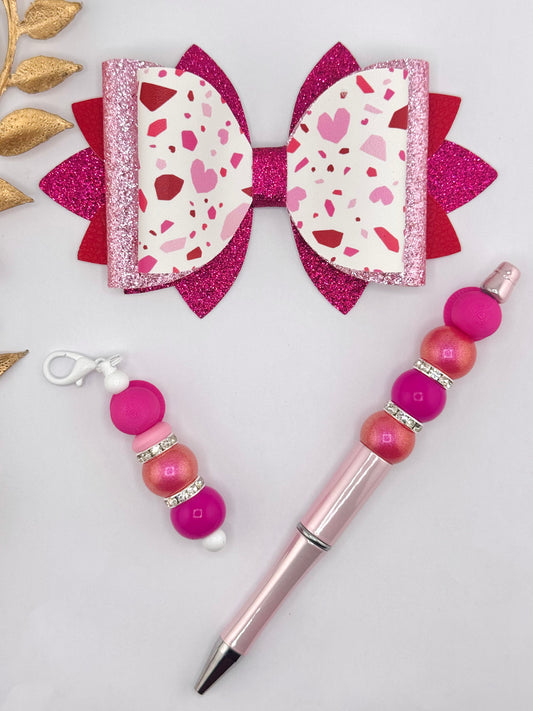 Pink terrazzo heart faux leather bow with layered hot pink and red glitter backing, Valentine-inspired handmade hair bow displayed with matching beaded pen and keychain.